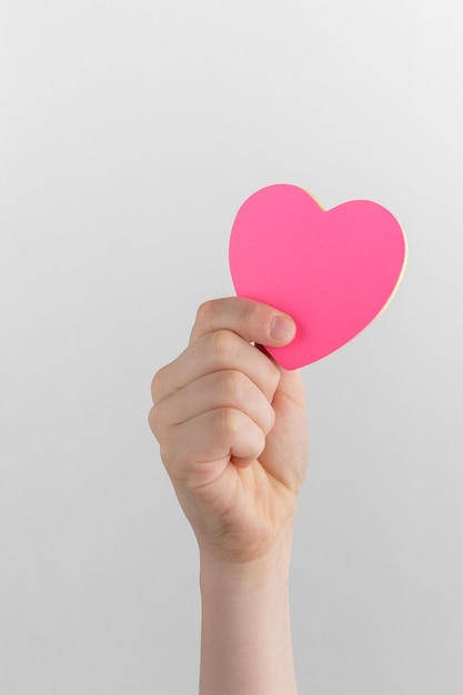 Child hand holding pink blank reminder or paper notes in the shape of a heart on a white background