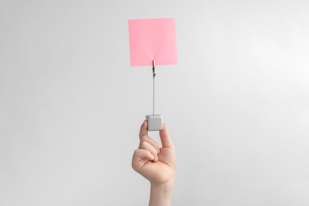 Child hand holding pink blank reminder or paper notes above a white and gray background copy space