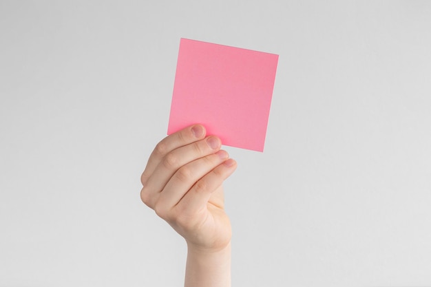 Child hand holding a square pink blank reminder or paper notes above a white and gray background