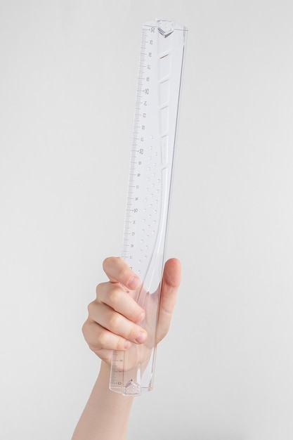 Child hand holding transparent glass or plastic ruler white and gray background with copy space