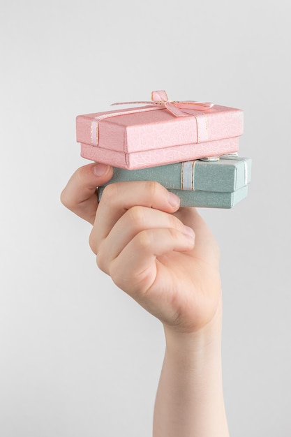 Child hand holding two gift boxes with pink and green bow white and gray background with copy space