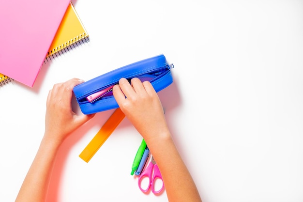 Child hand keeping all the pencils pens scissors etc in his pencil case Colorful notebooks