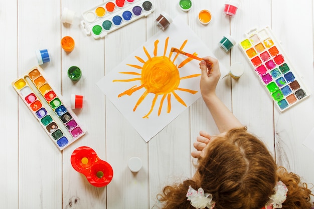 Child hand with brushes drawing on white paper yellow sun. 