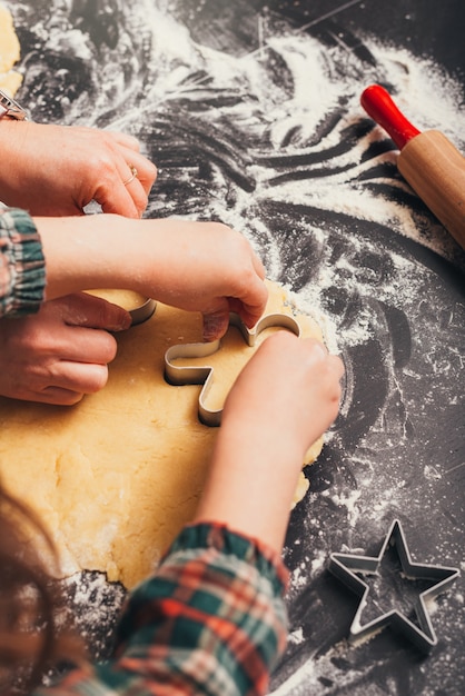 Child hands are cutting a heart shape from gingerbread dough.