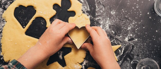 Child hands are cutting a heart shape from gingerbread dough.