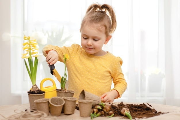 Child helping to care for indoor flowers and plants use yellow gardening tools