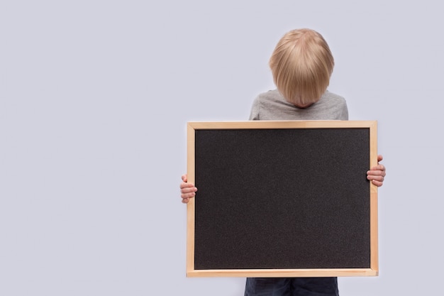 Child holding blackboard and looks at it. Copy space. Template. Mockup