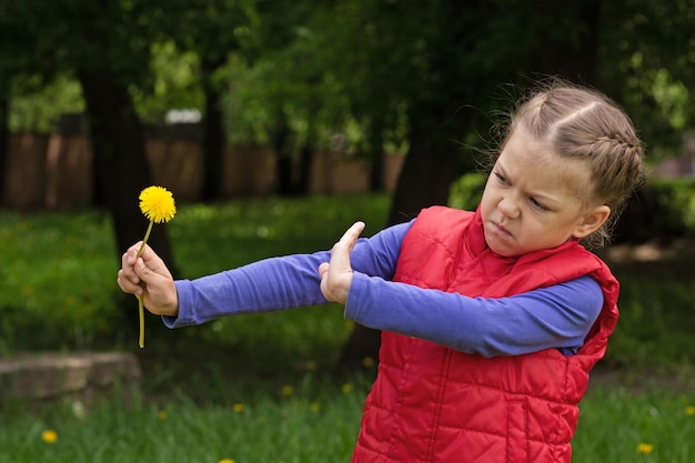 Child holding dandelion shown by hand against flower