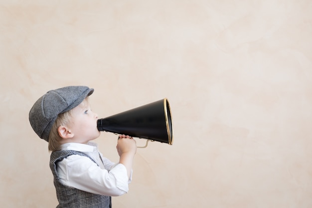 Child holding loudspeaker. Kid shouting through vintage megaphone. Business news concept