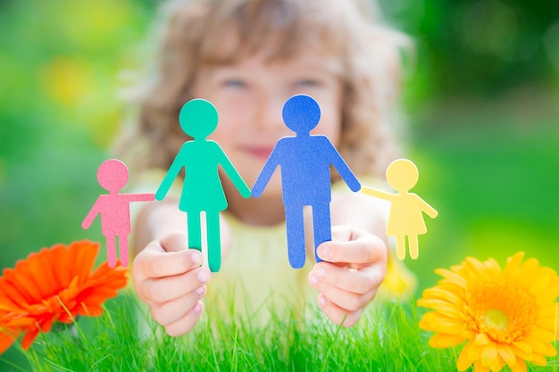 Child holding multi ethnic paper family in hands against spring green background