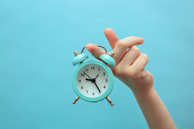 A child holds a small blue alarm clock