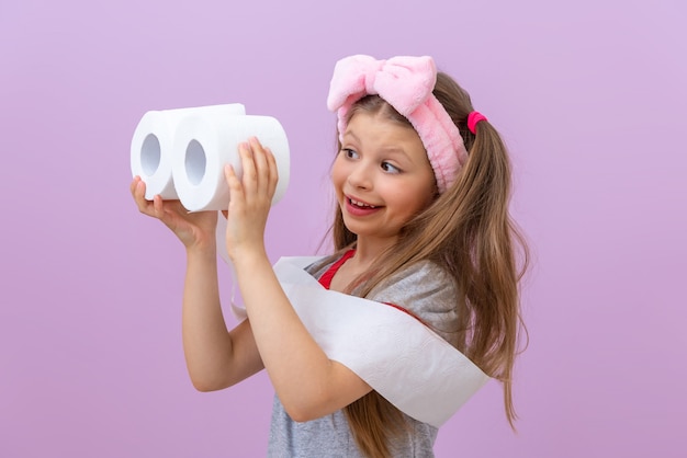 Child holds two rolls of toilet paper on light purple background