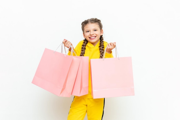 The child is happy with new purchases Shopping for children A beautiful little girl in a yellow tracksuit holds paper bags