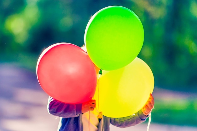 The child is hiding behind three balloons On the background of nature