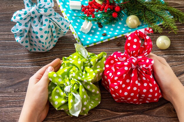 Child is holding Christmas gifts New year and gift wrapping zero waste furoshiki on wooden table