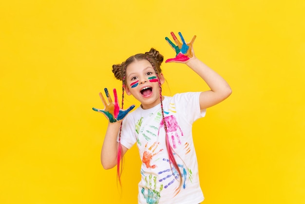 The child is playing with colorful paints A little girl stained with paint for drawing on a yellow isolated background Art courses for schoolchildren Creative education of children