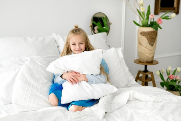 The child is sitting in bed with snowwhite bed linen hugging a large soft pillow