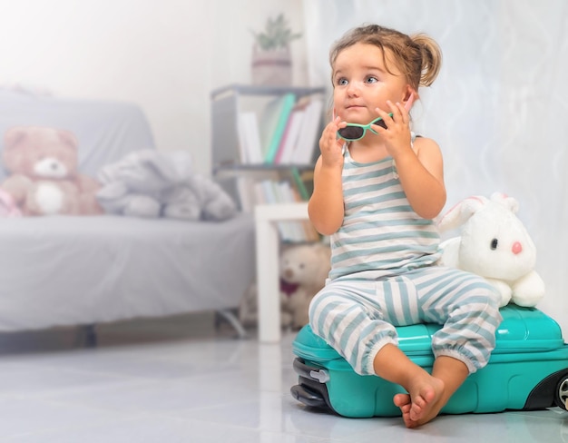 The child is sitting in sunglasses on a suitcase ready for vacation