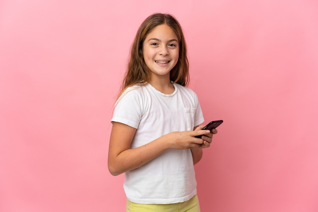 Child over isolated pink background sending a message or email with the mobile