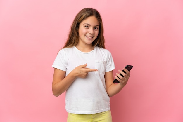 Child over isolated pink background using mobile phone and pointing it