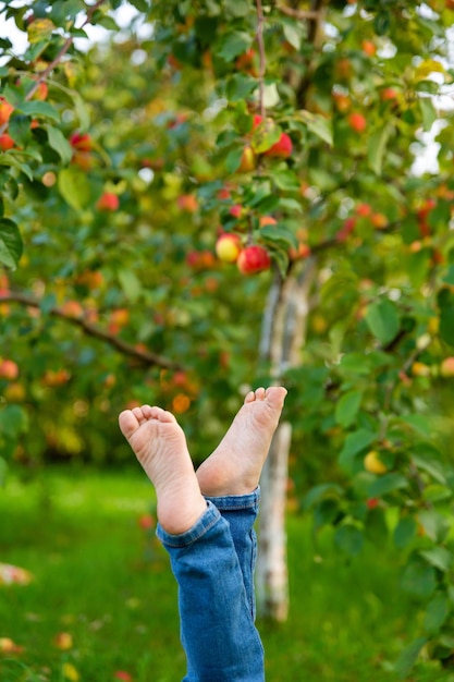 Child in jeans lifted up dirty barefoot against background of green leaves Hygiene and health