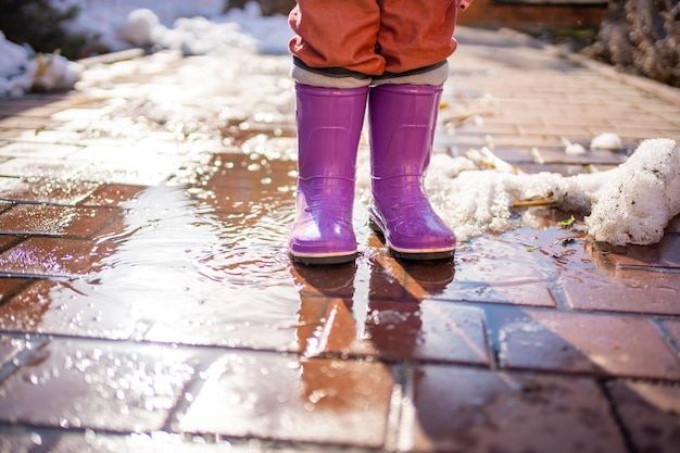 Child jumps on puddles in rubber boots at sunset lights in spring time