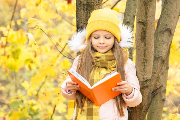 A child leans against a tree and reads the book autumn.