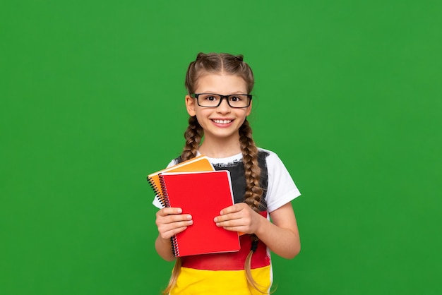 A child learns German on a green isolated background A beautiful little girl with glasses with a German flag and notebooks on a green isolated background