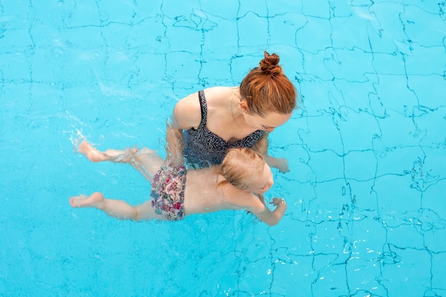 The child learns to swim. Mom and daughter are swimming in the pool. Top view. High quality photo