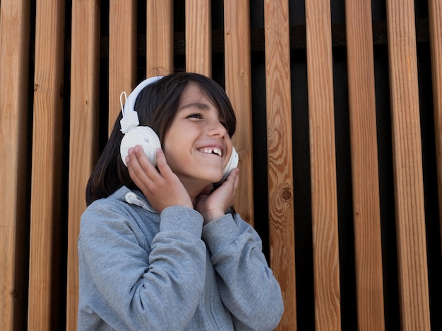 Child listening to music with white headphones in front of a wooden wall