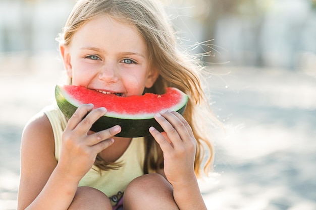 child little girl eat piece of juice watermelon on beach summertime and picnic outdoors