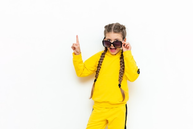 The child looks out from under sunglasses A beautiful little girl in a yellow summer suit on a white isolated background