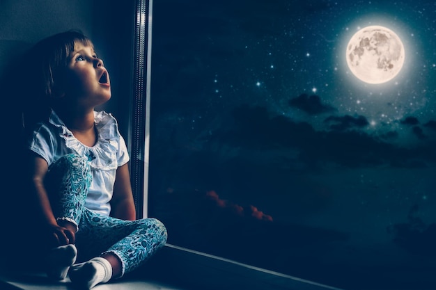 The child looks out the window into the night sky