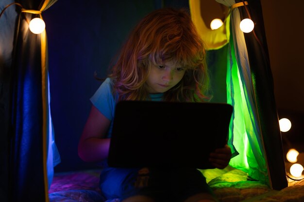 Child lying in bed and learning in virtual online school class kid working on laptop internet at hom