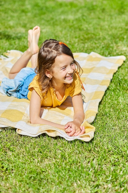 child lying on the blanket, on the grass in sun day, little girl take sunbathes on backyard house 