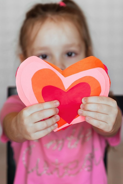 a child makes a holiday card with his own hands from paper hearts for Valentine's Day