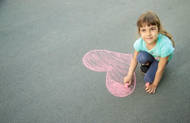 The child paints chalk on the asphalt heart Selective focus