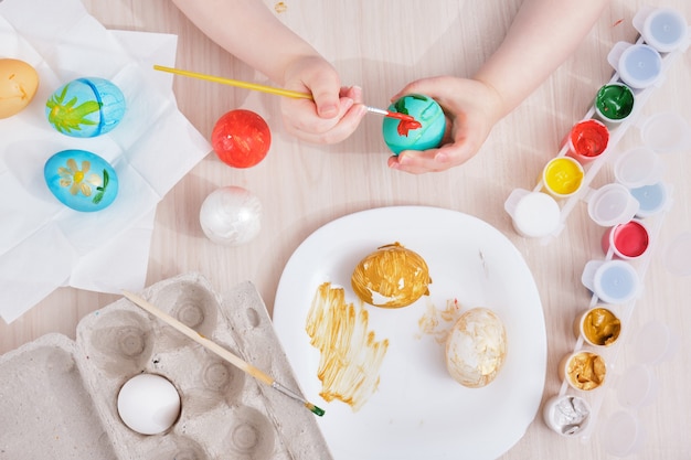 Child paints Easter egg on a wooden table