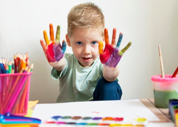 The child paints Palms and hands of a child in multicolored watercolor Watercolor gouache paint brushes colored and wax crayons stickers Set for drawing creativity and hobbies