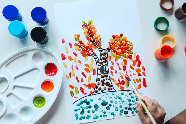 Child paints a tree with autumn leaves art concept