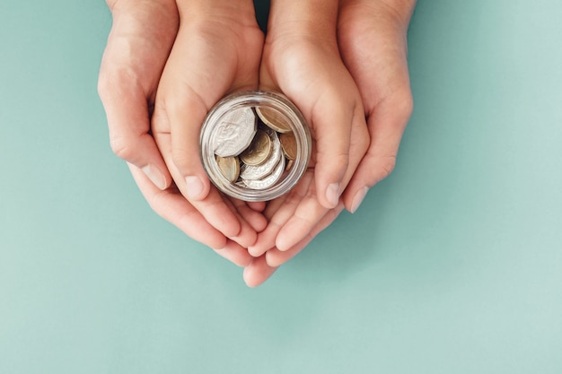 Child and parent hands holding money jar, donation, saving, family finance plan concept