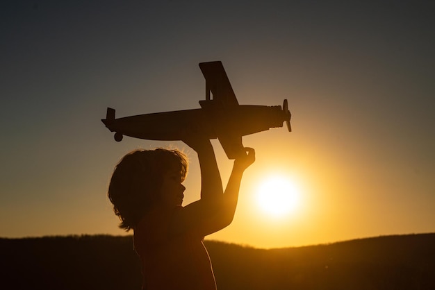 Child pilot aviator with toy airplane dreams of traveling in summer in nature at sunset