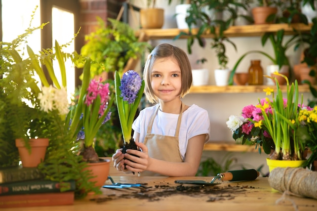 Child planting spring flowers. Little girl gardener plants hyacinth. Girl holding hyacinth in flower pot. Child taking care of plants. Gardening tools. Copy space.