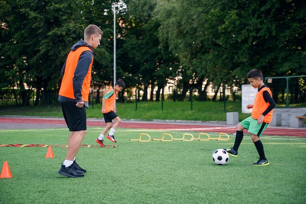 Child player in football uniform working out the kicking ball together with coach