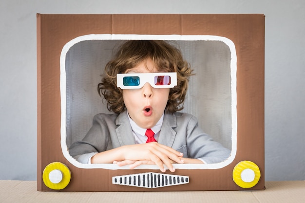 Child playing with cardboard box TV. Kid having fun at home. Communication concept