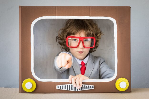 Child playing with cardboard box TV. Kid having fun at home. Video blogging concept