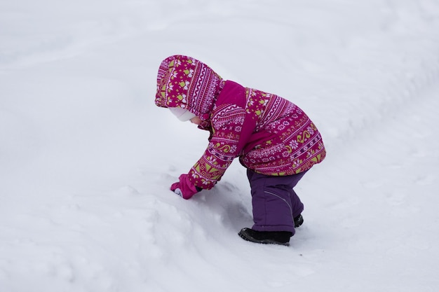 Child playing with snow in snowy park in winter