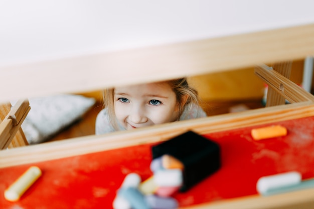 Child plays hide and seek. The child hid behind the drawing board in the nursery. Visible only happy face