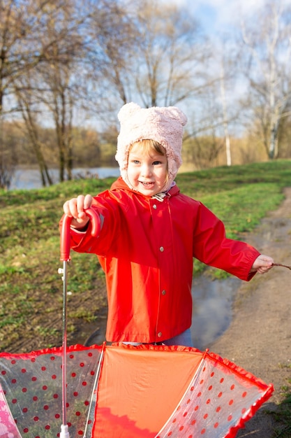 Child plays with umbrella after the rain in red rubber boots and a raincoat