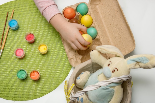 Child puts painted Easter eggs in a basket next to a brush and paint and an Easter bunny